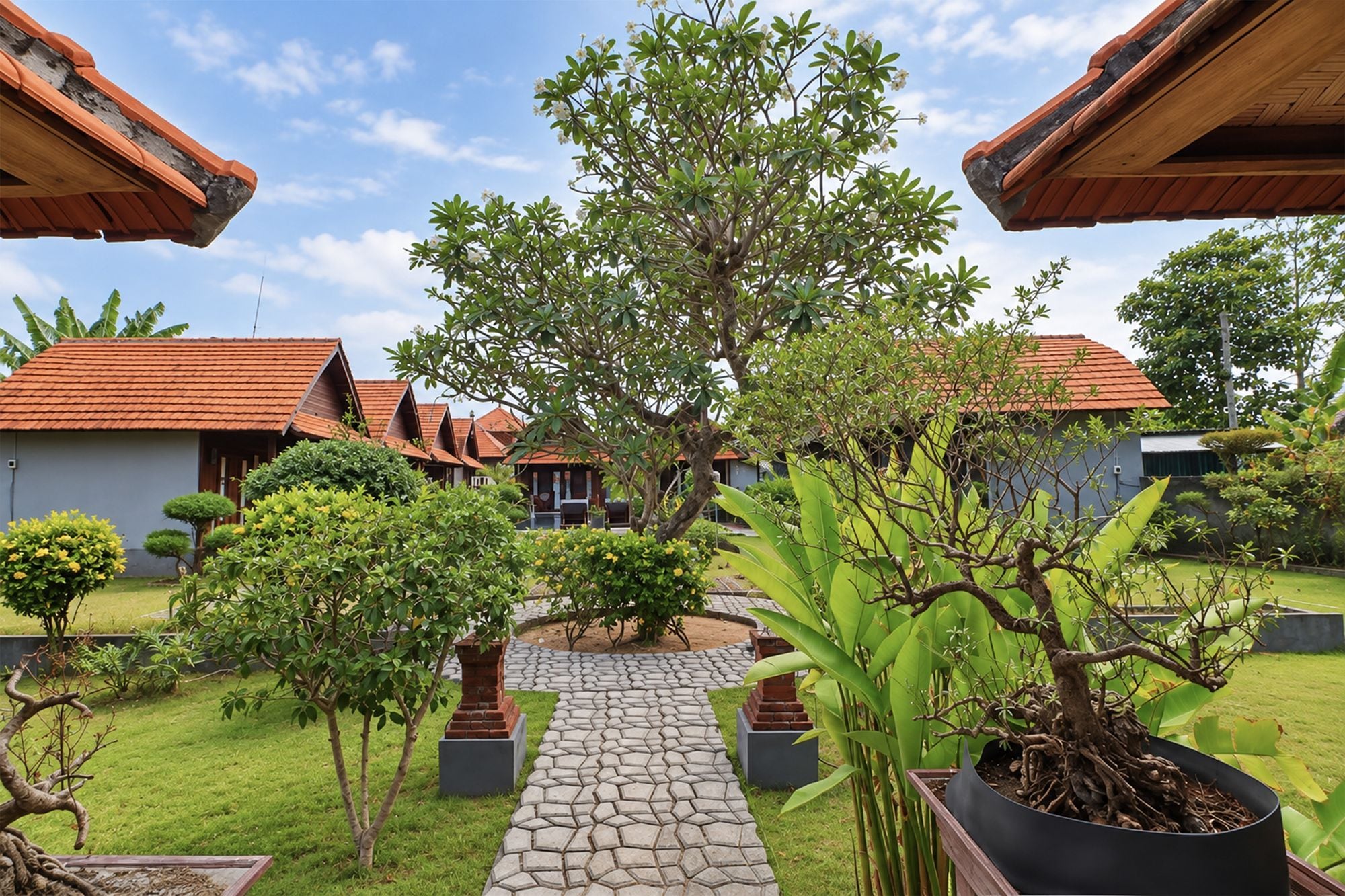 A courtyard with a stone pathway, potted plants, and traditional-style buildings with red-tiled roofs.