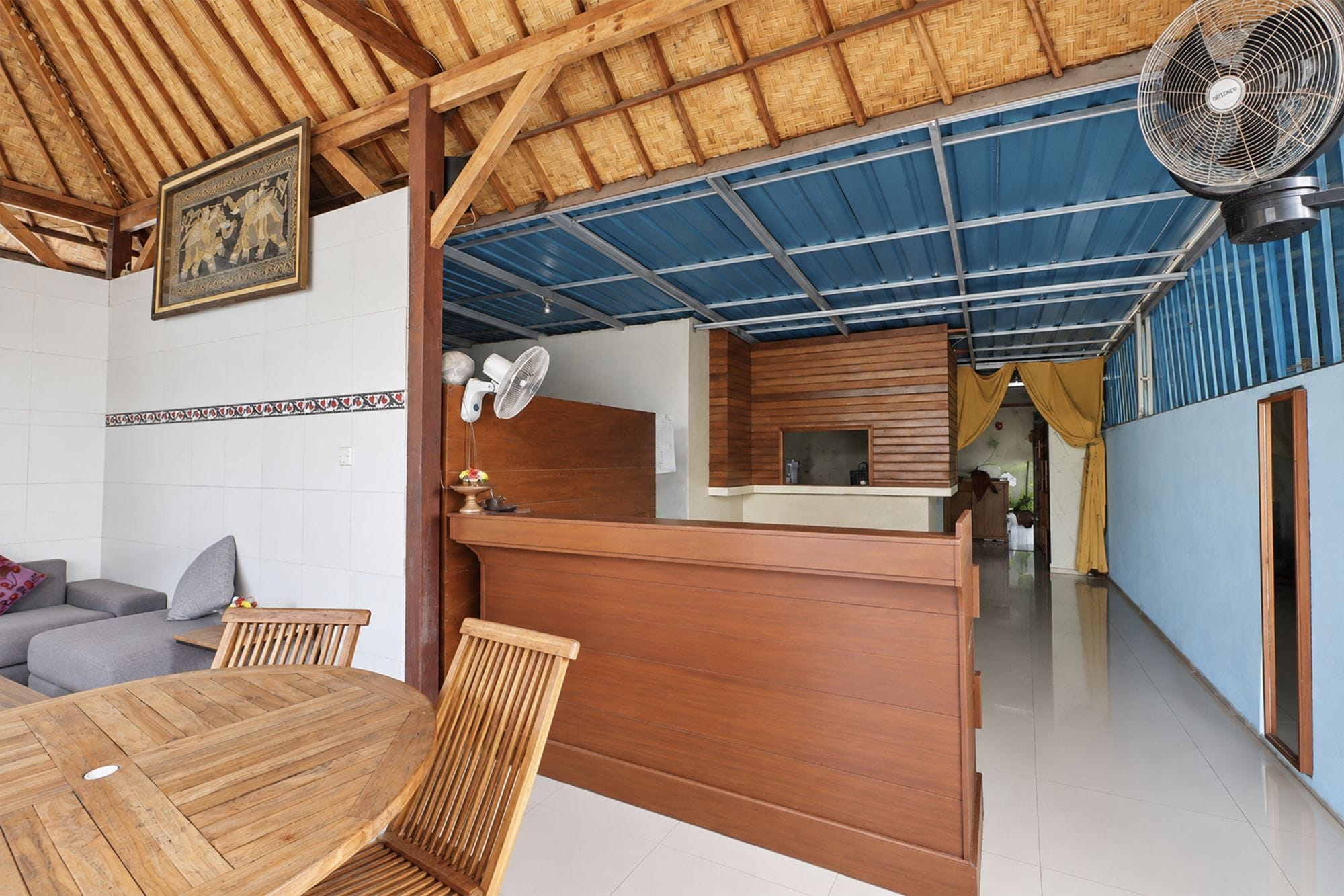 Una habitación con una mesa de comedor de madera, sillas, un ventilador de techo, una zona de cocina y vistas al exterior.