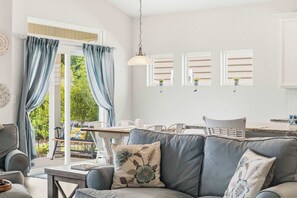 Ein modernes Wohnzimmer mit grauem Sofa, einem Esstisch und einer Küchenzeile mit weißen Schränken.