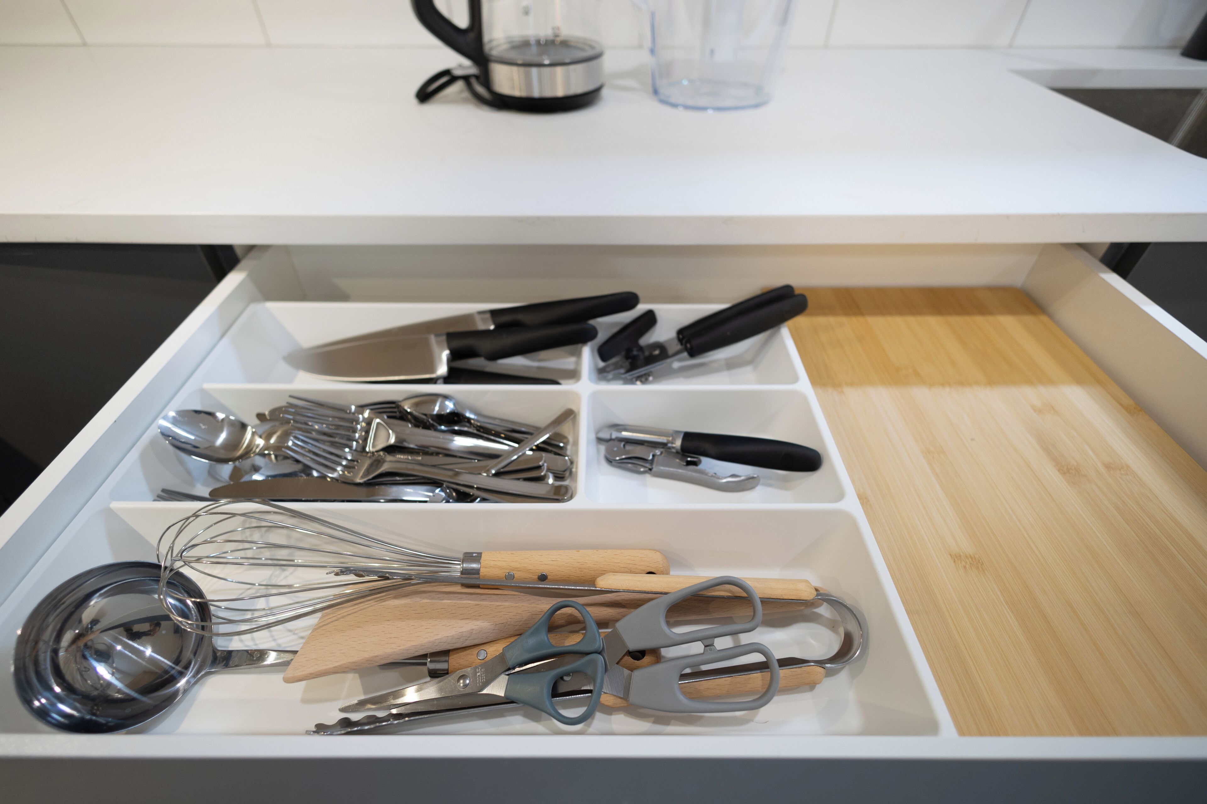 A kitchen drawer with utensils and a cutting board.