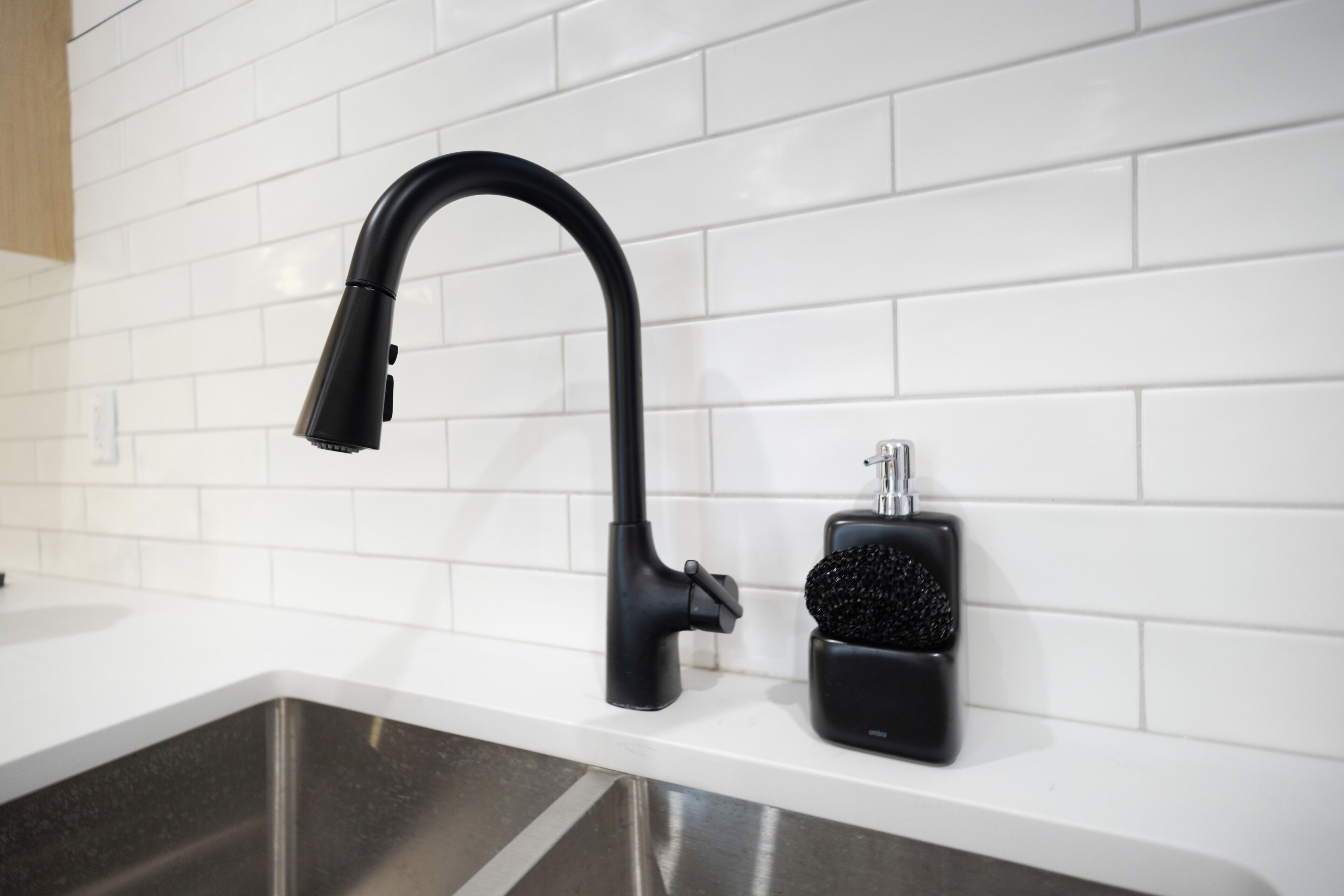 A modern kitchen with a black faucet, a stainless steel sink, and a black soap dispenser.