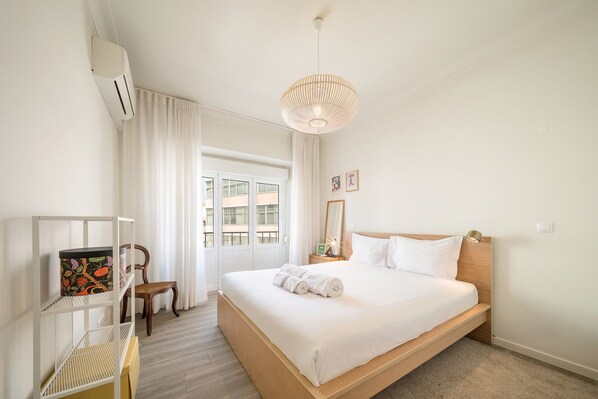 Ein Schlafzimmer mit Bett, einem Sessel, einem Regal mit Dekoration, einer Hängelampe und einer Tür zum Balkon.