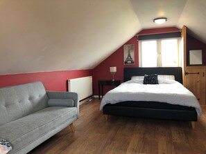 A bedroom with a bed, a sofa, a radiator, a lamp, and a window.