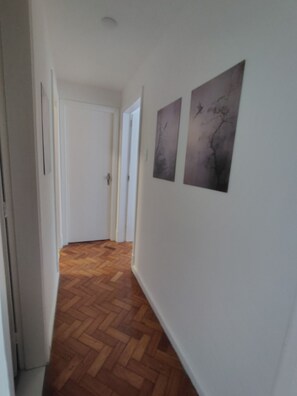 Ein Flur mit Holzboden, weißen Wänden und zwei gerahmten Bildern.