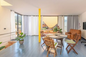 A modern living room with a dining area, large windows, a sofa, and a TV. - Casa Galería, encanto en la Costa Brava (Ullà)