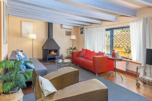 Een woonkamer met een open haard, een bank, een rode slaapbank en een televisie.