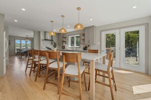 A modern kitchen with wooden chairs, pendant lights, and a large window.