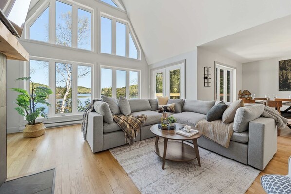 A spacious living room with a large sectional sofa, a coffee table, and a view of a lake through large windows.