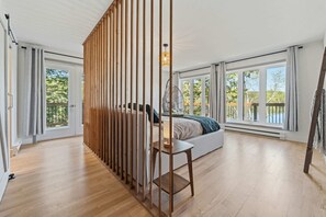 A bedroom with a large bed, a wooden partition, and a view of the outdoors.