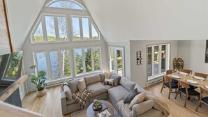 A spacious loft with a large window, a cozy sectional sofa, a dining table set for four, and a television in the corner.