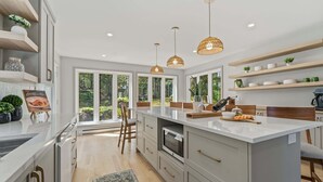 A modern kitchen with a large island, pendant lights, and a view of the outdoors.