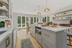 Cocina moderna con una isla grande, luces colgantes y vistas al exterior.