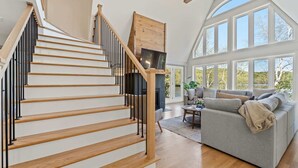 A staircase with wooden steps and black railings, a gray sofa, and large windows.