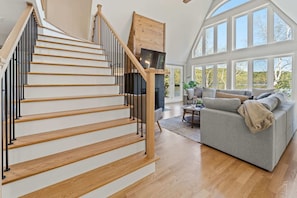 A staircase with wooden steps and black railings, a gray sofa, and large windows.