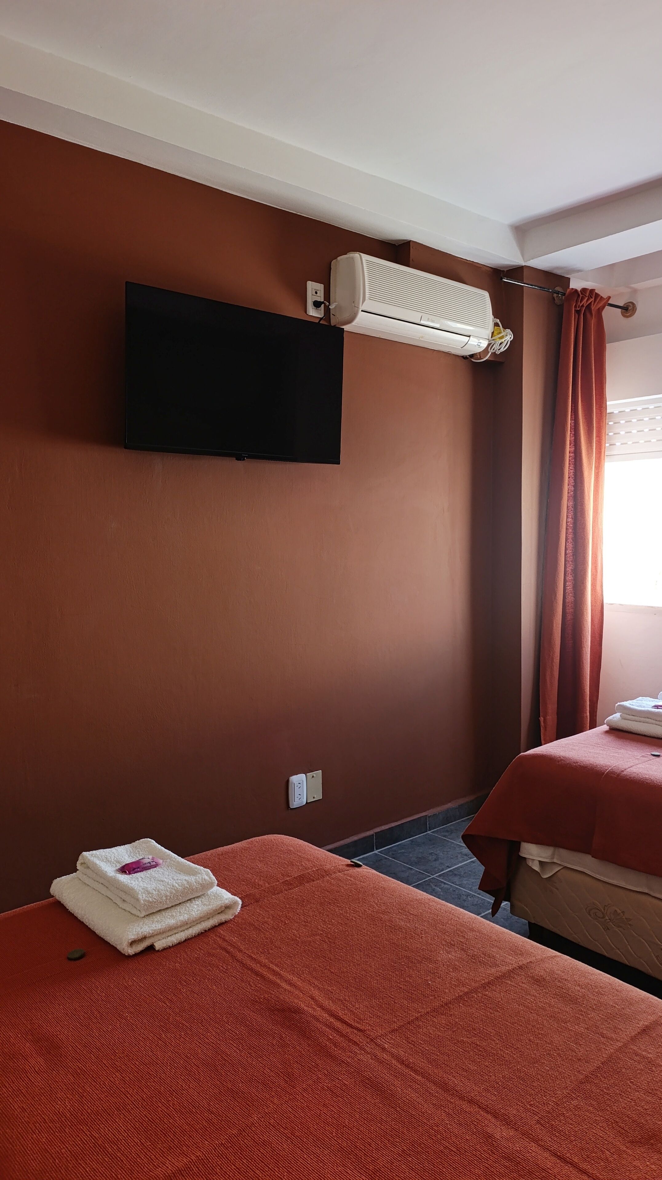 A hotel room with two beds, an air conditioner, a TV, and a window with curtains.