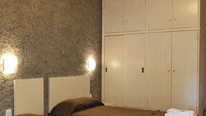 A hotel room with two beds, a wardrobe, and wall-mounted lights.