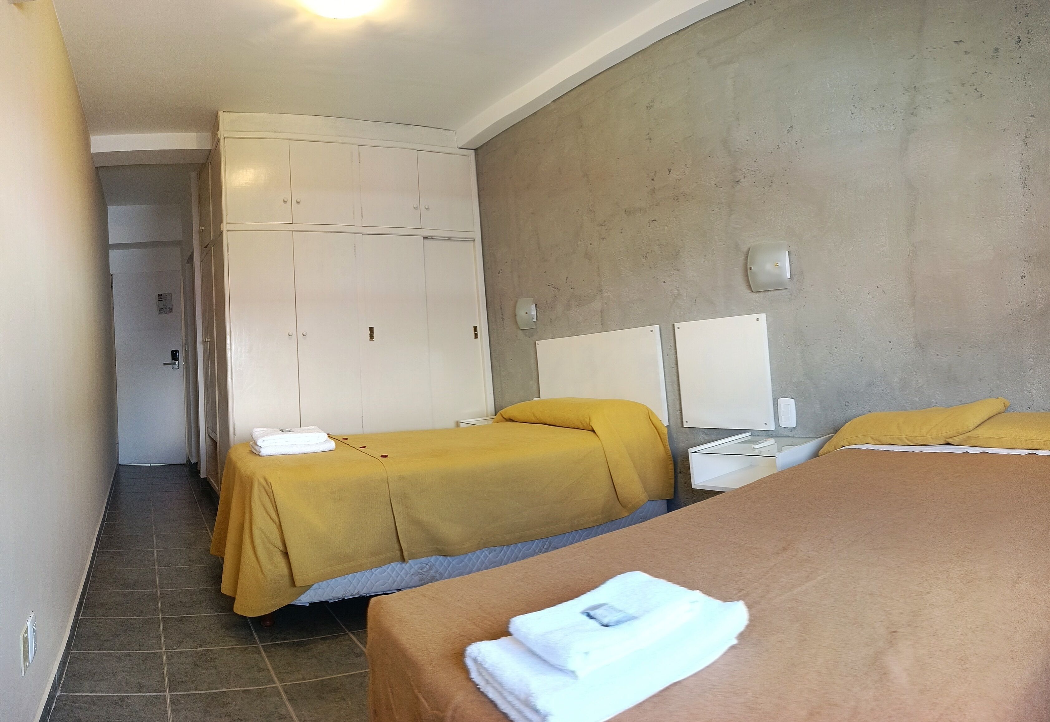 Una habitación de hotel con dos camas, un armario y un baño visible al fondo.