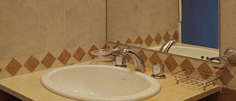 Un baño con un lavamanos blanco, un espejo y una lámpara sobre el espejo.