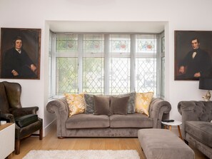 Ein Wohnzimmer mit grauem Sofa, zwei Sesseln, einem Holztisch und zwei Bildern an den Wänden.