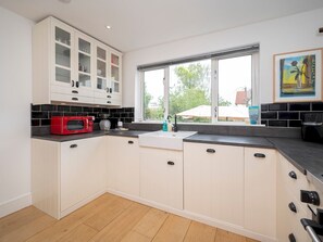 A kitchen with white cabinets, a red microwave, a sink, and a window with a view of greenery. - Stylish House - 25mins London Bridge train journey - Pass the Keys (London)