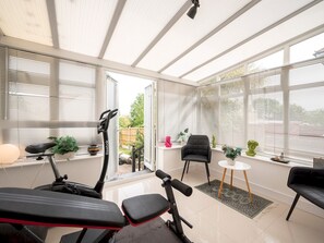 Ein Wintergarten mit Trainingsgeräten, einer Sitzecke und großen Fenstern.