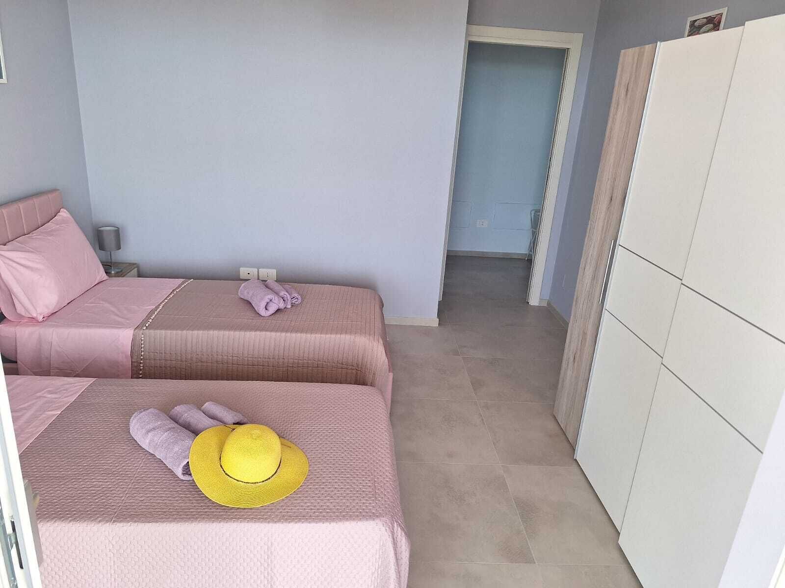 A bedroom with two beds, a wardrobe, and a bathroom visible in the background.