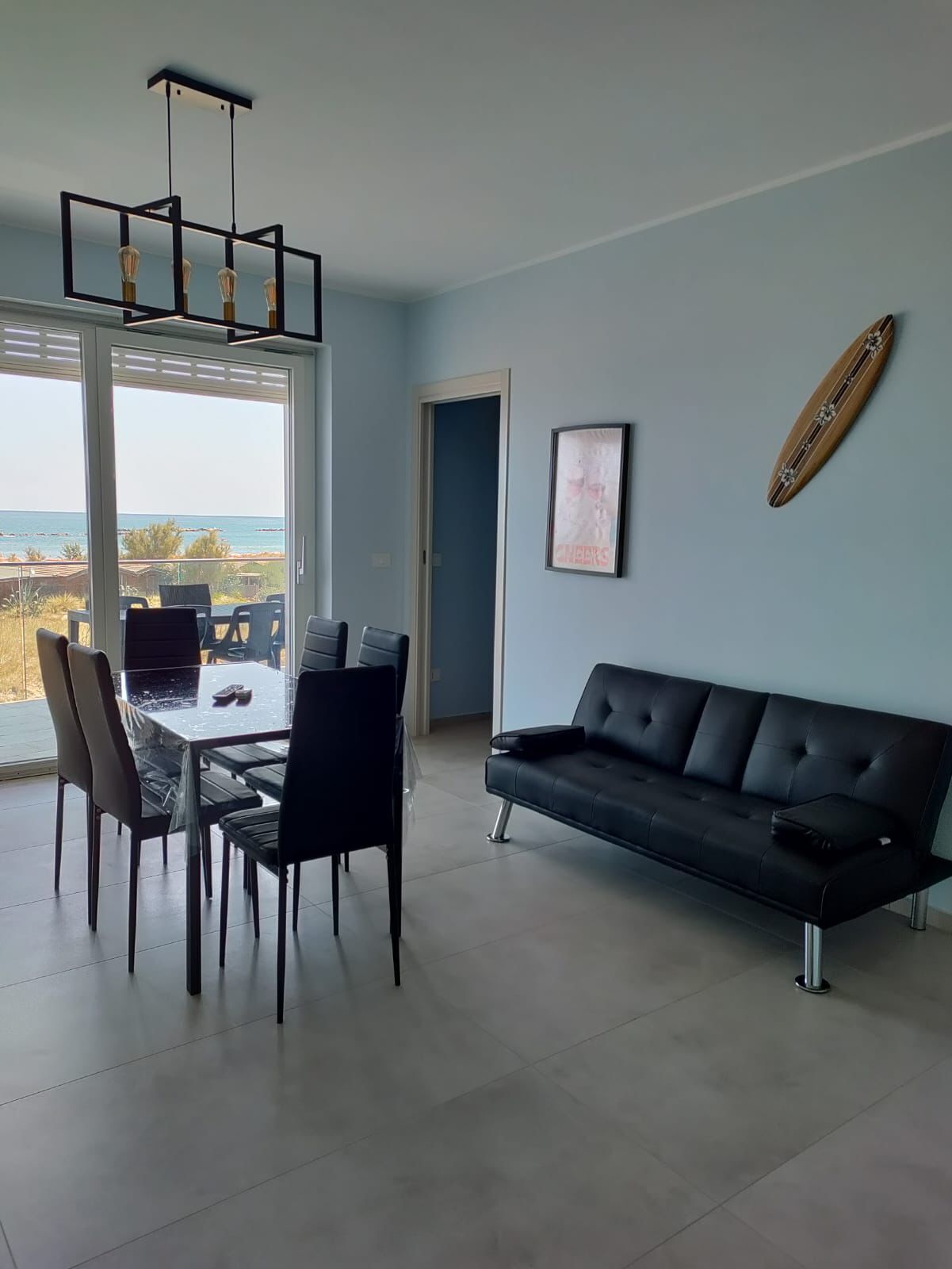 Een moderne woonkamer met een eettafel, stoelen, een zwarte leren bank, een hanglamp en uitzicht op de oceaan.