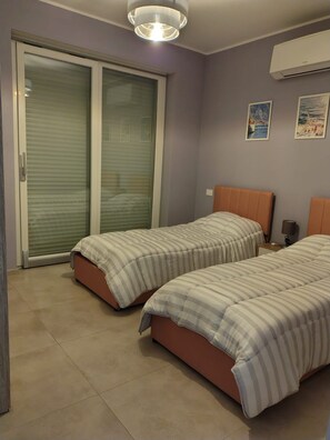 A bedroom with two beds, a sliding glass door, an air conditioner, and two wall-mounted paintings. - WoW Sea view 2-bedroom in lovely Campomarino Lido at the beach! (Campomarino Lido)