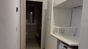 Ett tvättrum med en tvättmaskin, ett torkställ och en dörr som leder till ett annat rum.