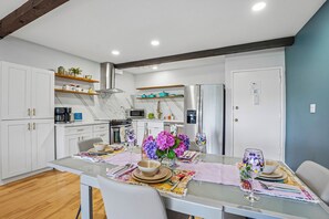 Eine moderne Küche mit weißen Schränken, einem Edelstahl-Kühlschrank und einem Essbereich mit Tisch, Stühlen und Dekoration.