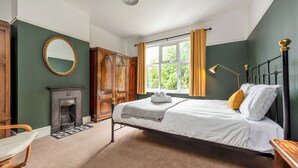 Une chambre à coucher avec un lit, un miroir, une cheminée et une fenêtre avec des rideaux.