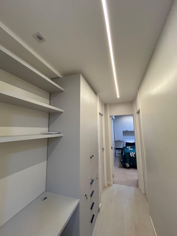A narrow hallway with built-in shelving, a door leading to a bedroom, and a kitchenette area. - Fully Furnished Apartment in Manaus (Manaus)