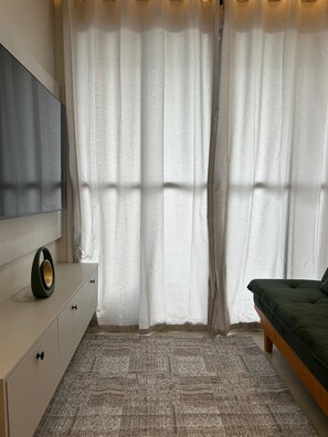 A bedroom with a bed, a TV on a dresser, a patterned rug, and sheer curtains. - Fully Furnished Apartment in Manaus (Manaus)