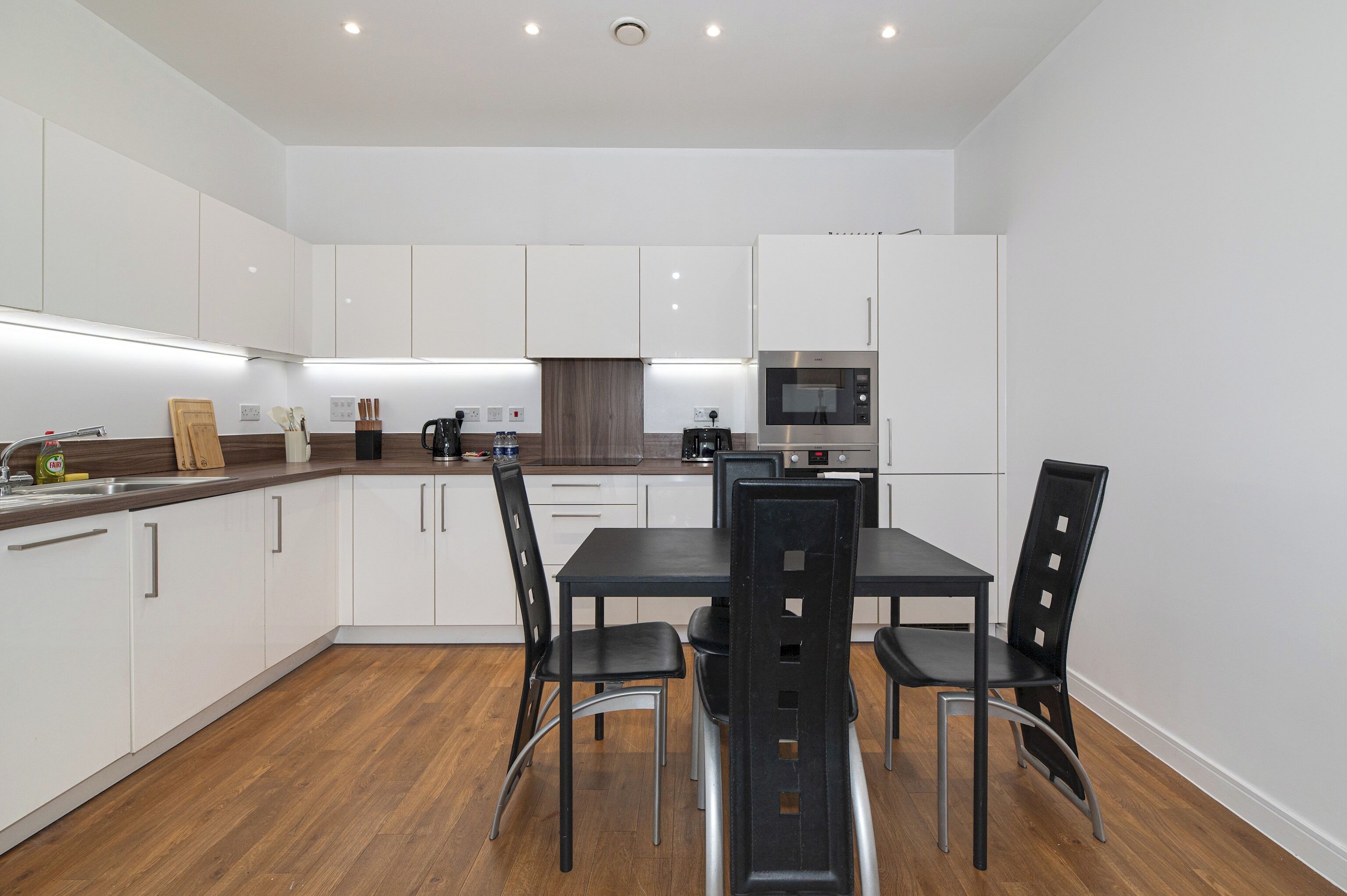 Une cuisine moderne avec des meubles blancs, une table à manger avec des chaises et un four encastré.