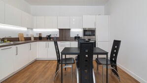 A modern kitchen with white cabinets, a dining table with chairs, and a built-in oven. - Modern 2BR flat with Balcony, in East London - Pass the Keys (London)