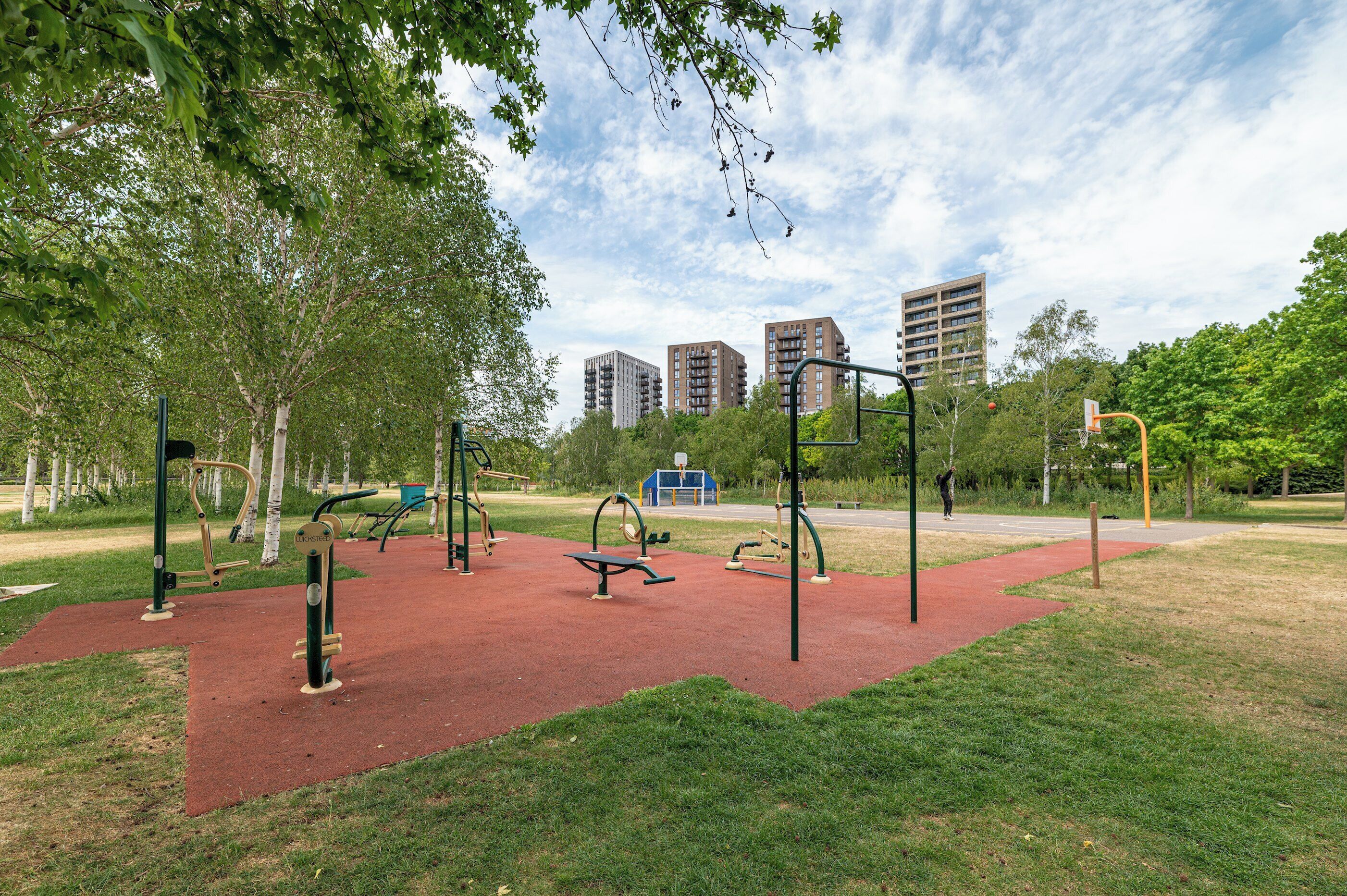 An outdoor exercise area with equipment, trees, and buildings in the background.