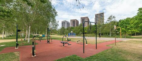 An outdoor exercise area with equipment, trees, and buildings in the background.