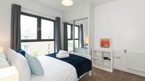 A hotel room with a bed, a white console table, a radiator, and large windows with curtains. - Modern 2BR flat with Balcony, in East London - Pass the Keys (London)
