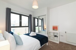 Ein Hotelzimmer mit einem Bett, einem weißen Konsolentisch, einem Heizkörper und großen Fenstern mit Vorhängen.