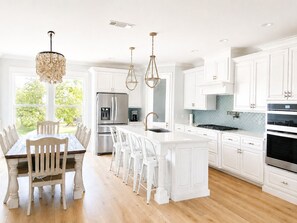 A modern kitchen with white cabinetry, a central island, stainless steel appliances, and pendant lighting.