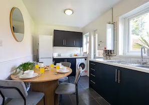Eine moderne Küche mit dunklen Schränken, einem Essbereich mit rundem Tisch und einem großen Fenster für natürliches Licht.