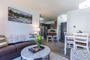Una sala de estar moderna con un sofá marrón, una mesa redonda de centro con mandos a distancia y un cuadro en la pared.