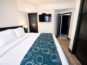 Ein Hotelzimmer mit einem Bett, einem an der Wand montierten Fernseher und einer Tür zu einem weiteren Raum.