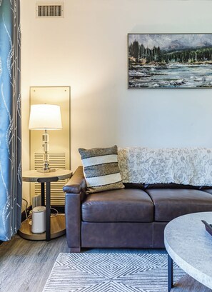 Ein modernes Wohnzimmer mit einer Ledersofa, einem runden Couchtisch, einer Stehlampe und einem Bild an der Wand.