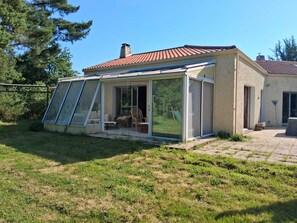 Une maison dotée d’un patio fermé par des baies vitrées, d’une cheminée et d’une cour dallée.