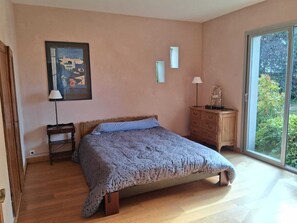 Une chambre à coucher avec un lit, une commode, une lampe, un tableau encadré et une grande fenêtre.