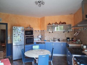 Une cuisine compacte équipée d’un réfrigérateur, d’un four, d’un four à micro-ondes et d’un évier. On y trouve une table à manger avec des chaises et un pare-feu en carrelage.