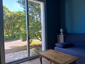 A room with a sliding glass door leading to a garden, a blue sofa, and a small wooden table. - Family home in the heart of the Nantes vineyards (Vertou)