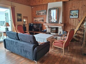 Un salon chaleureux avec une cheminée, des murs en bois, un canapé, des fauteuils et un téléviseur.