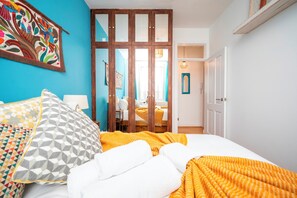 Un dormitorio con cama, almohadas, un separador de madera y un colorido cuadro en la pared.